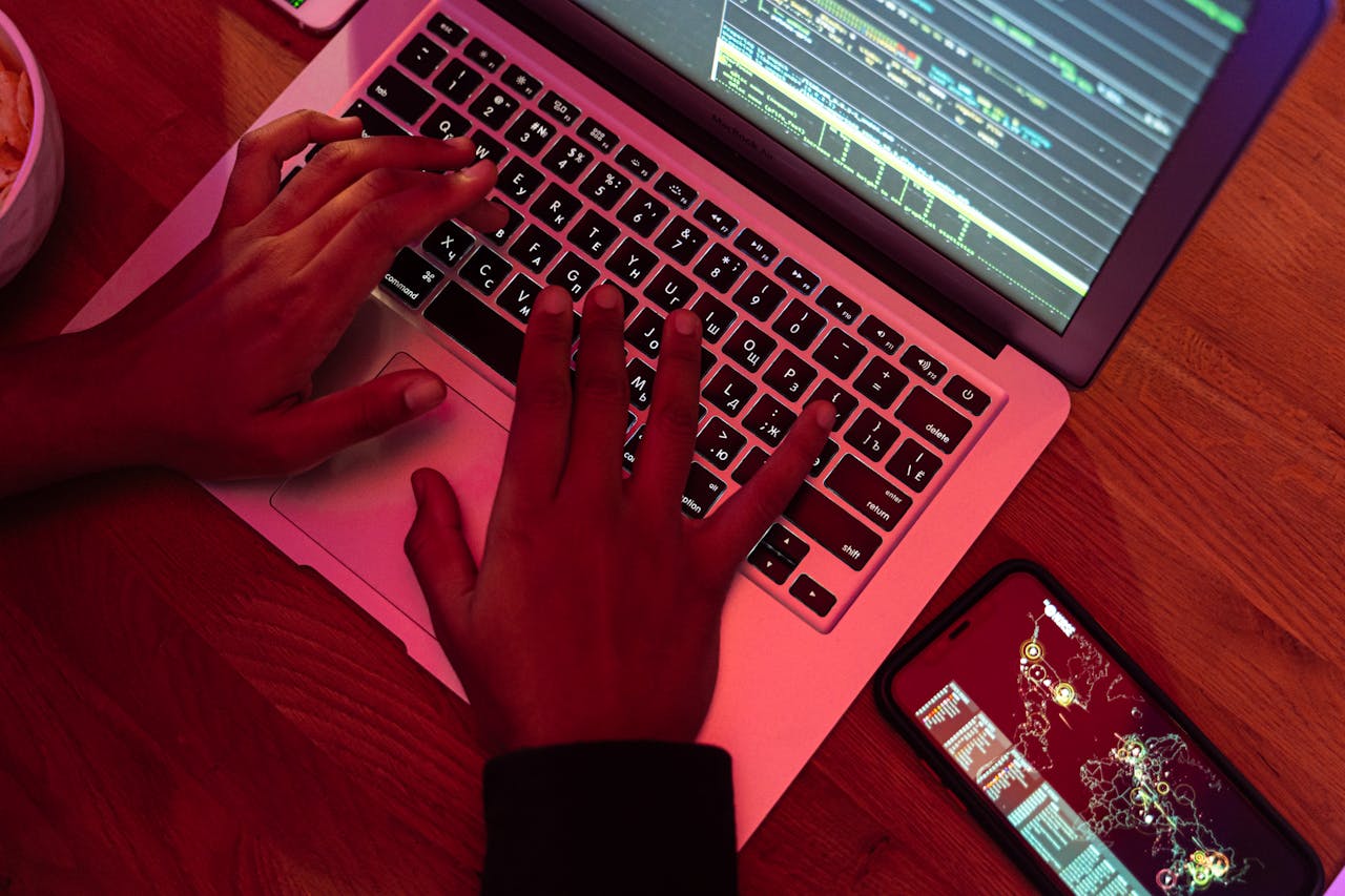 portfolio-07 Hands typing on a laptop with code on screen, smartphone nearby at night, indoor setting.
