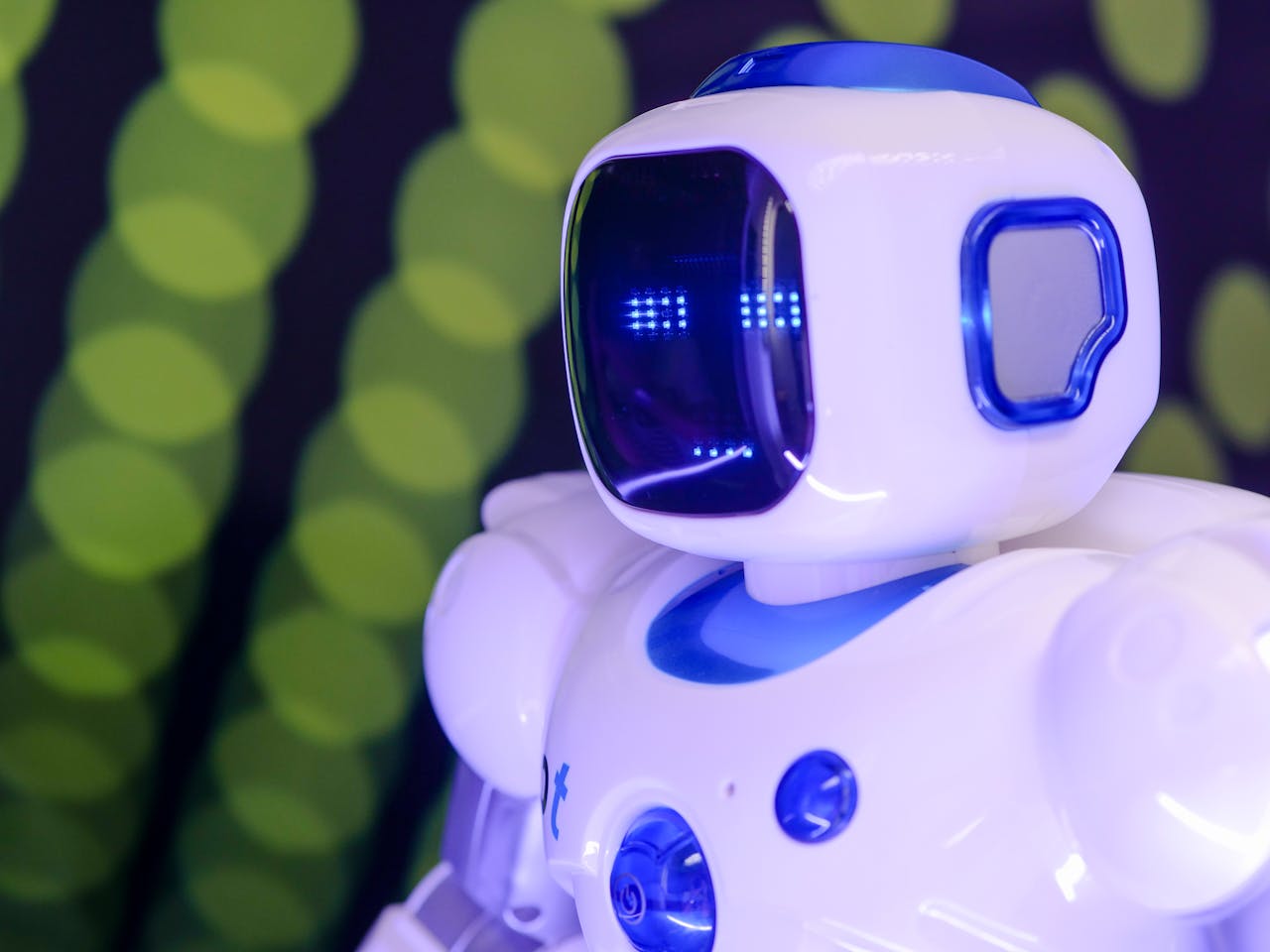 our-story-01 Close-up of a modern humanoid robot with glowing blue features on a green abstract background.